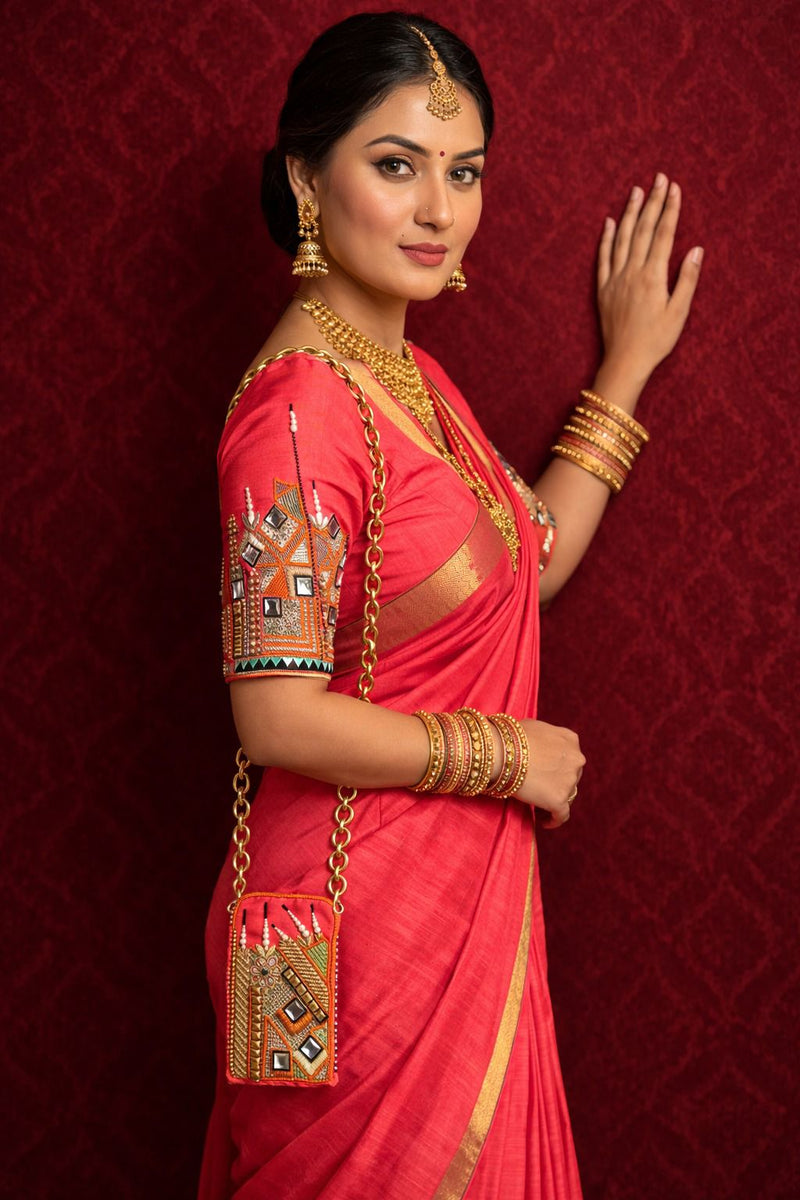 Model in a coral-pink saree with mirror-work sleeve embroidery, small chain sling bag at her hip