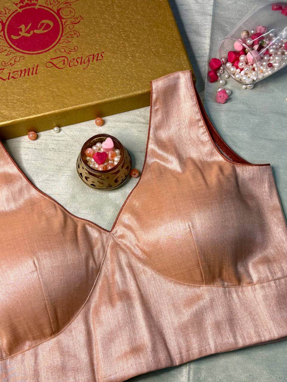 Rose gold shimmer blouse laid flat, sleeveless with a V-neck, gold gift box behind