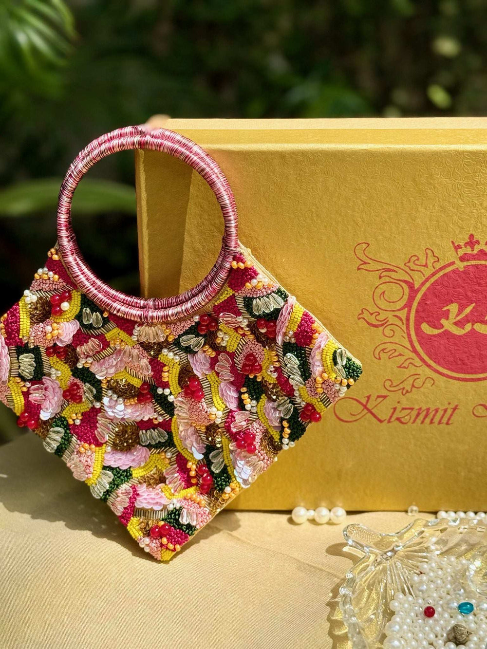 Diamond-shaped clutch in pink, yellow and green threadwork with ring handles, by a gold box