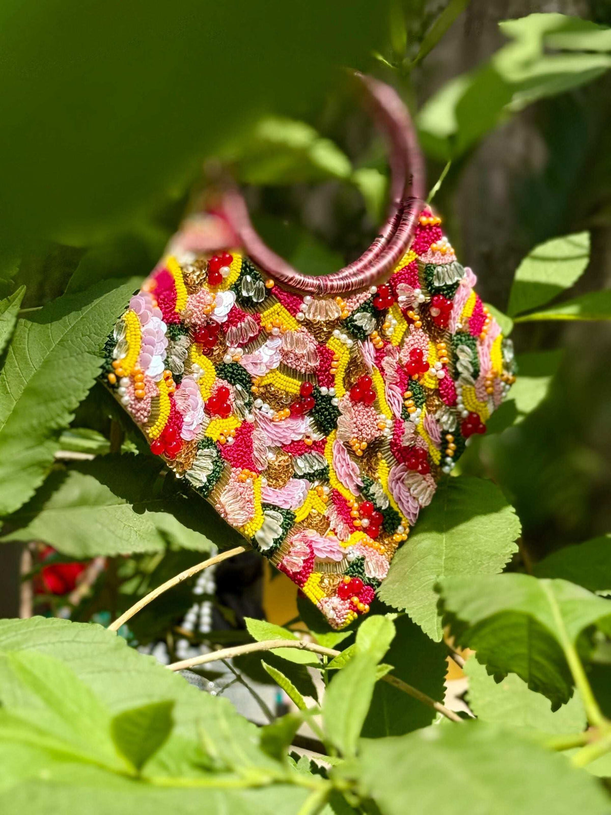 Pink and yellow beaded clutch with twin ring handles, photographed among garden leaves