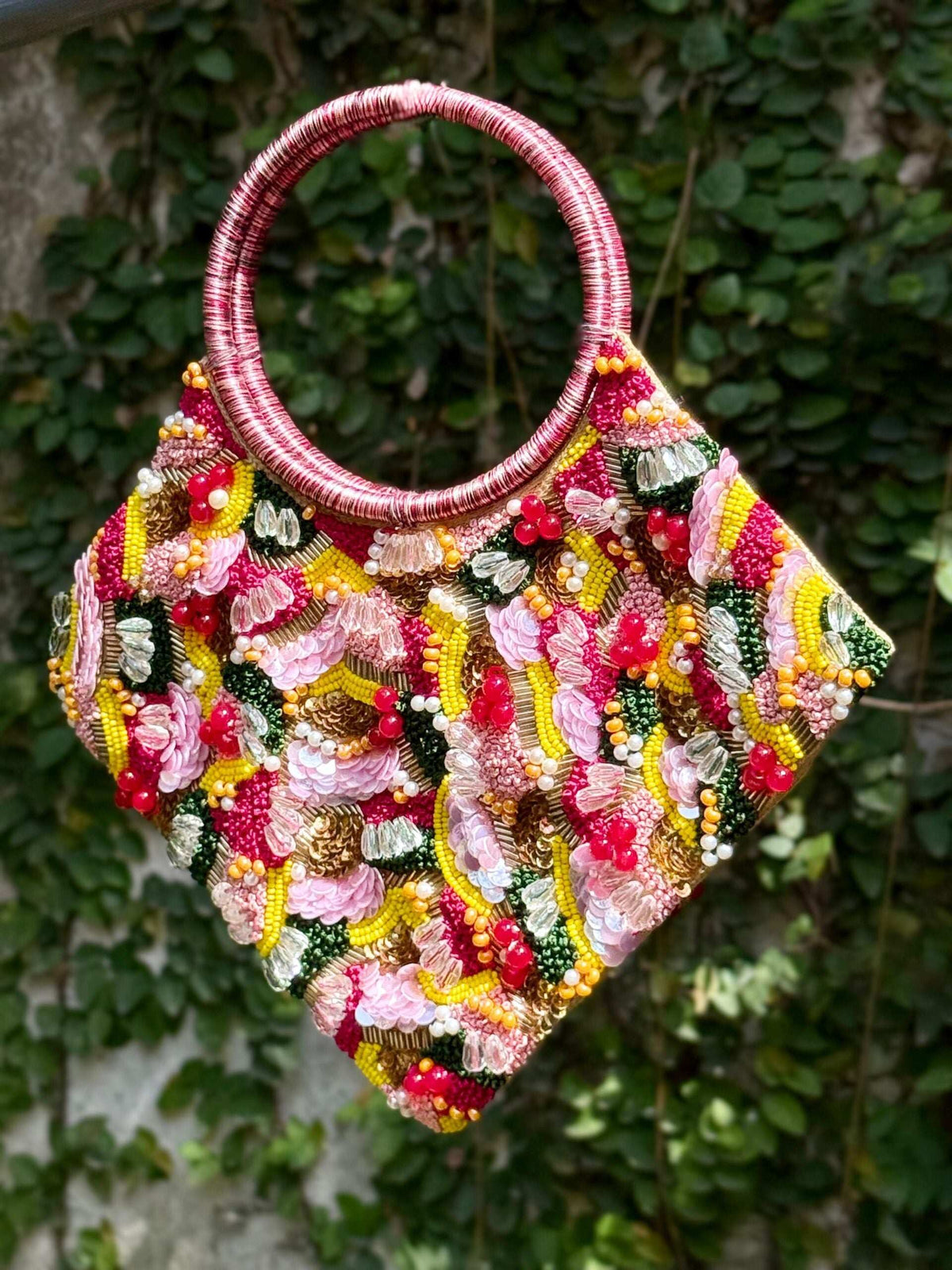 Clutch front in dense pink, yellow and green beadwork, shown against a leafy wall