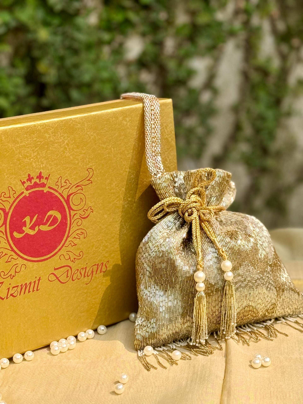 Gold potli drawn shut with a gold cord and pearl-tipped tassels, beside a gift box
