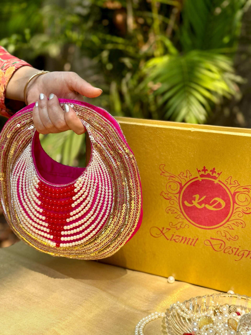 Pink and gold sequinned round clutch held by its cut-out handle beside a gold gift box